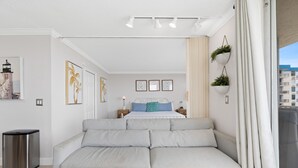 A modern bedroom with a large bed, a sofa, and a trash bin. - Estero Beach & Tennis 901-c (Fort Myers Beach)