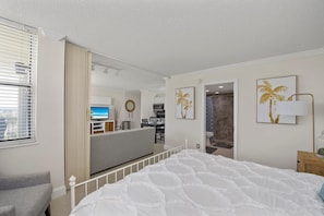 Relax in a stylish space with a large bed, sofa, and dining area, surrounded by artwork and a window with a view.
