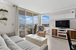 A modern living room with a sofa, a chair, a TV, and a balcony with a city view.