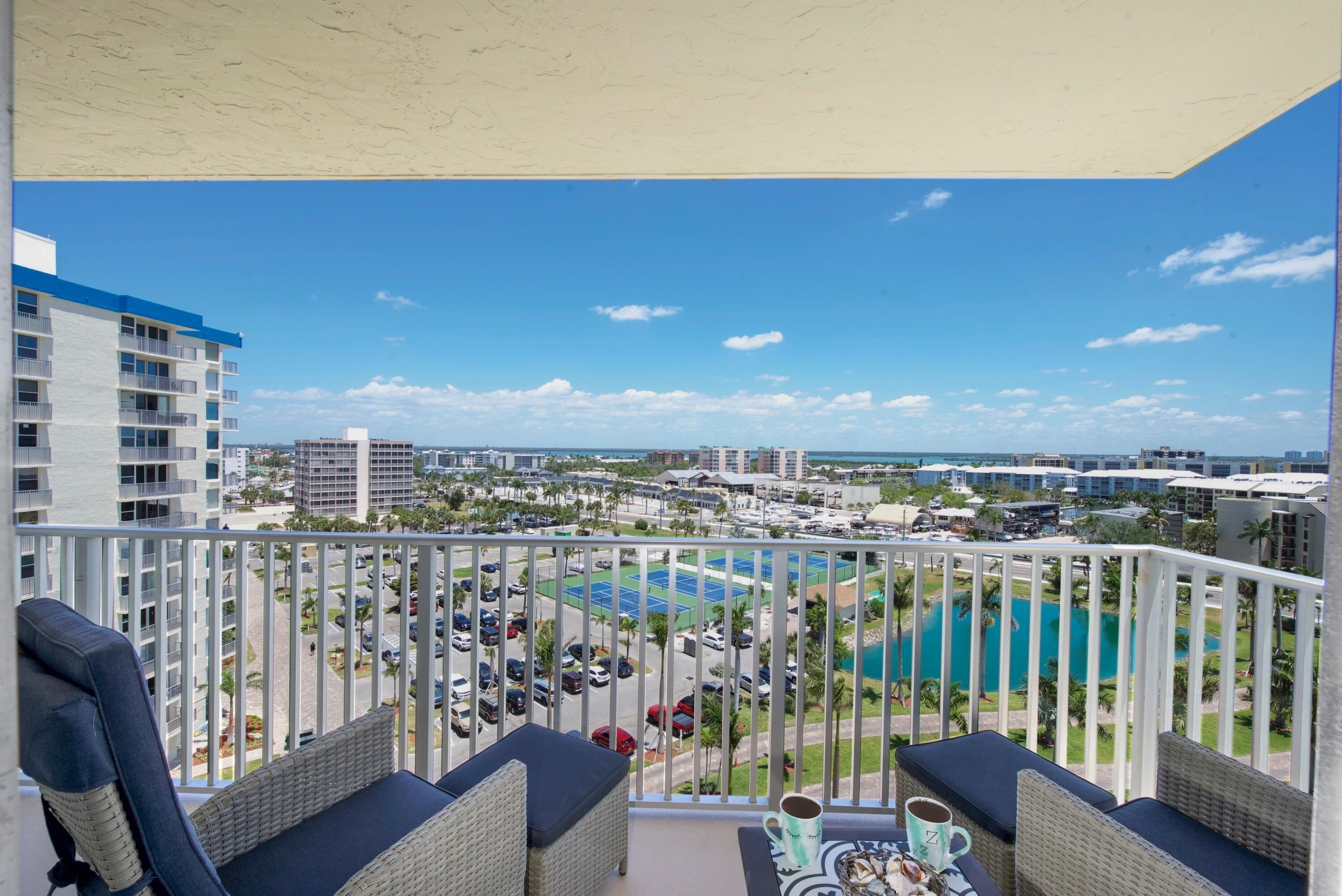 Ein Balkon mit Korbmöbeln, Blick auf einen Swimmingpool und die umliegenden Gebäude.