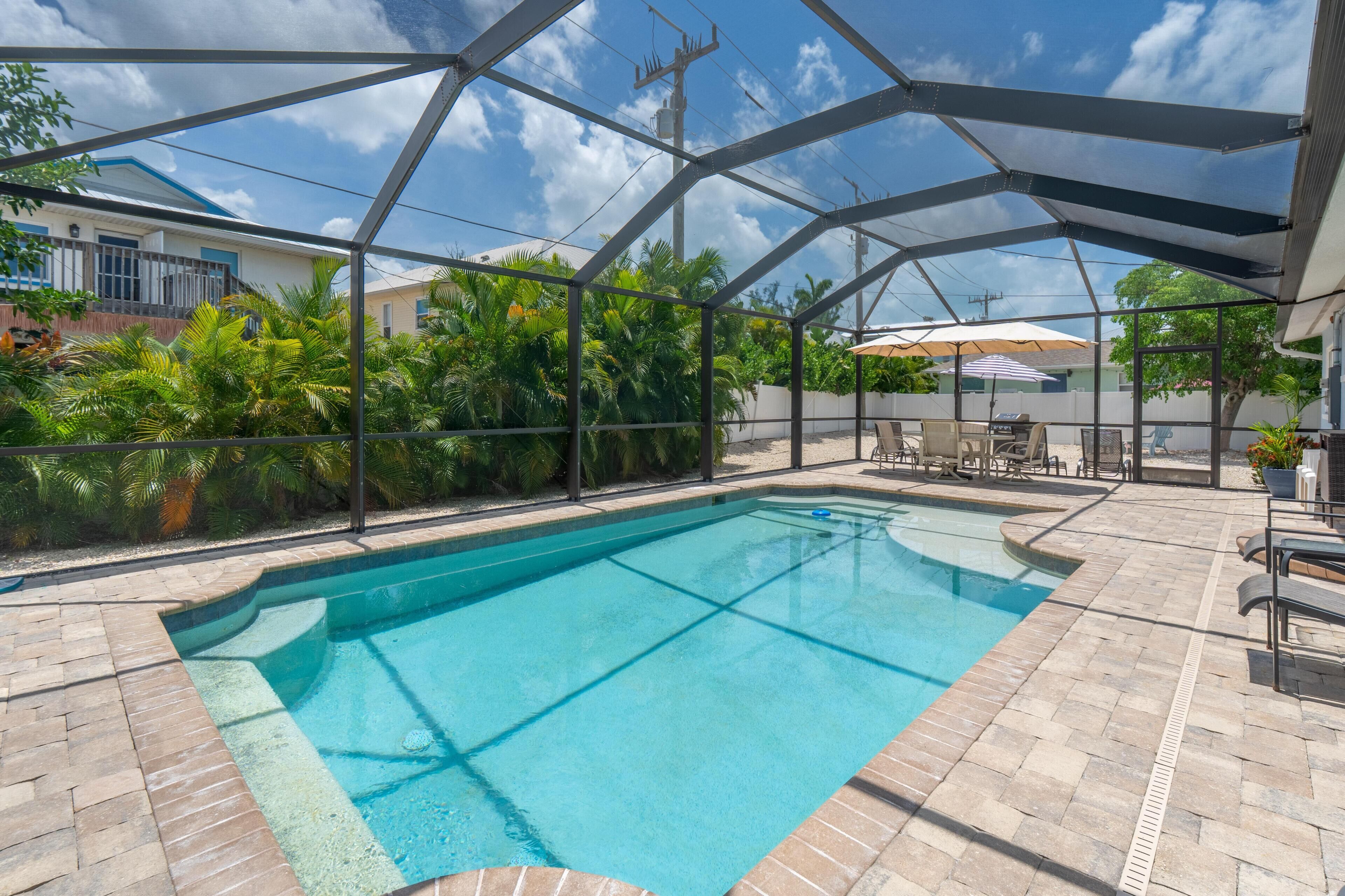 Une piscine dotée d’un patio couvert, entourée d’une végétation luxuriante et surplombée d’un ciel bleu azur.