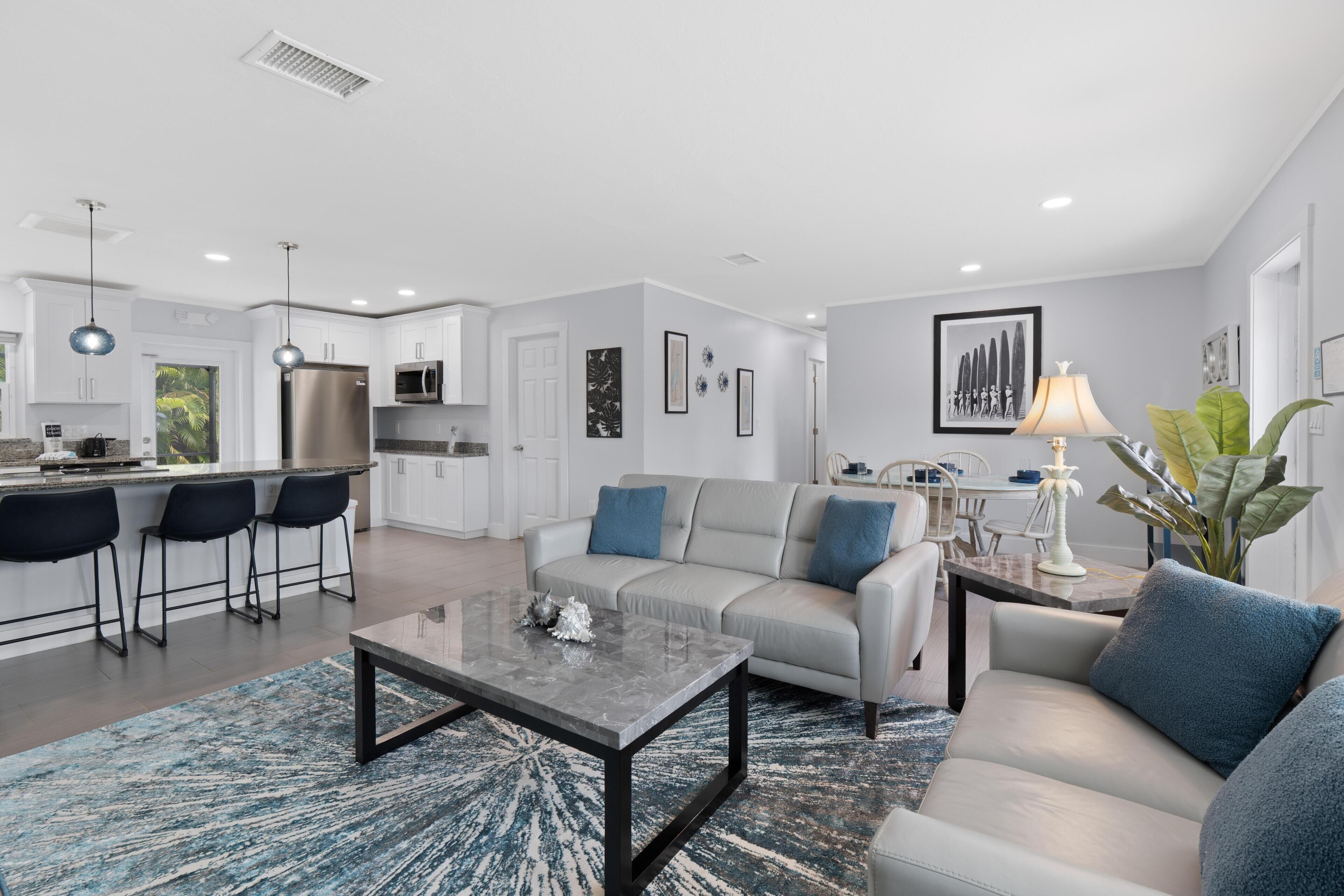 A modern living room with a sofa, coffee table, and a kitchen area with a refrigerator and microwave.