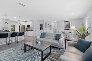 A modern living room with a sofa, coffee table, and a kitchen area with a refrigerator and microwave. - Ocean Breeze (Fort Myers Beach)