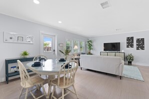 A modern living room with a dining area, a sofa, a TV, and decorative plants. - Ocean Breeze (Fort Myers Beach)