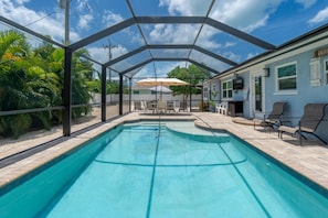Una piscina techada con zona de patio, sillas de descanso y una mesa con sombrillas.