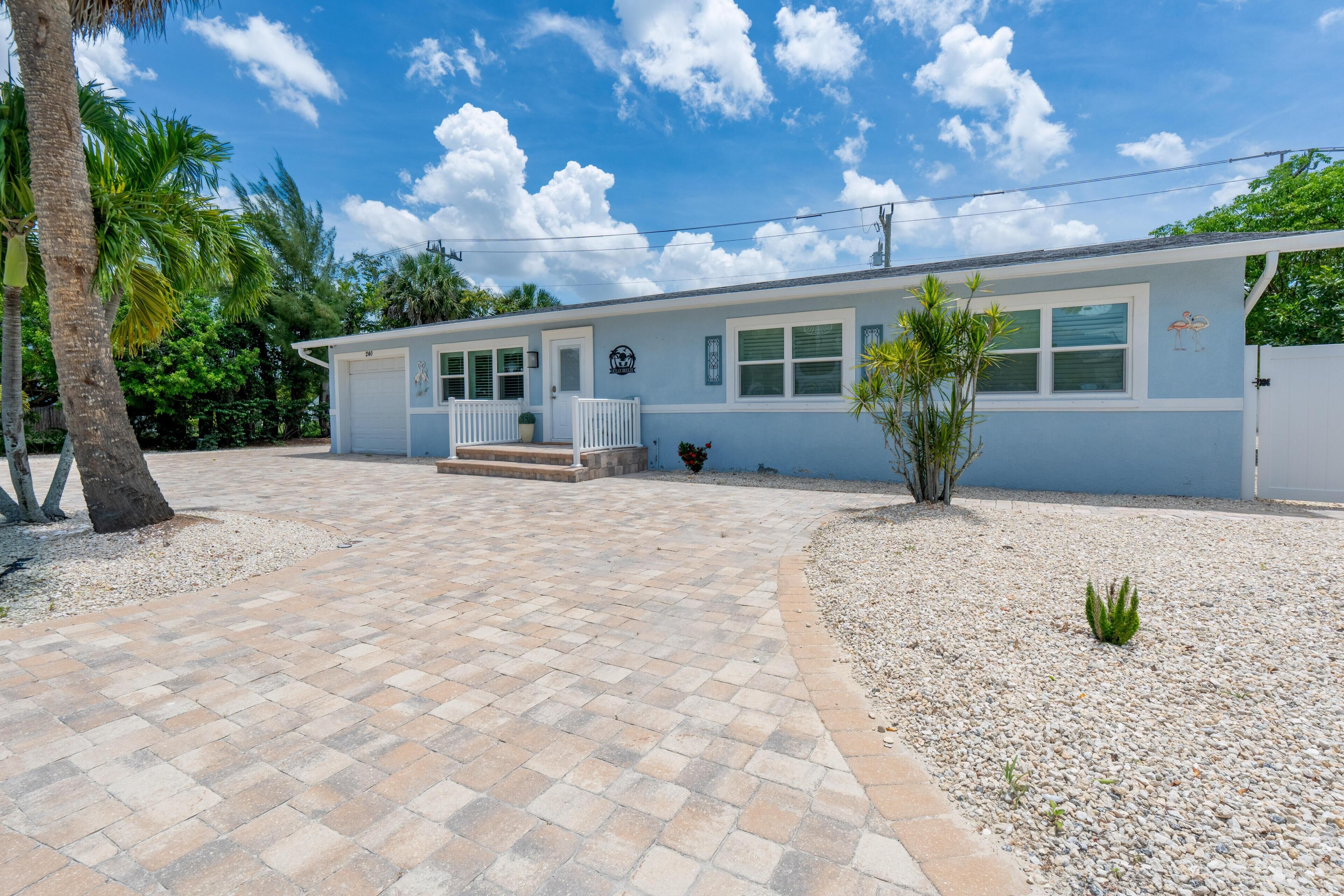 A single-story building with a front porch, a small garden area with a palm tree, and a clear blue sky.