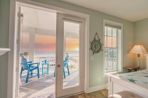 A room with a view of the ocean, a door leading to an outdoor deck with chairs, and a lamp by the window. - Sunset Paradise (Fort Myers Beach)