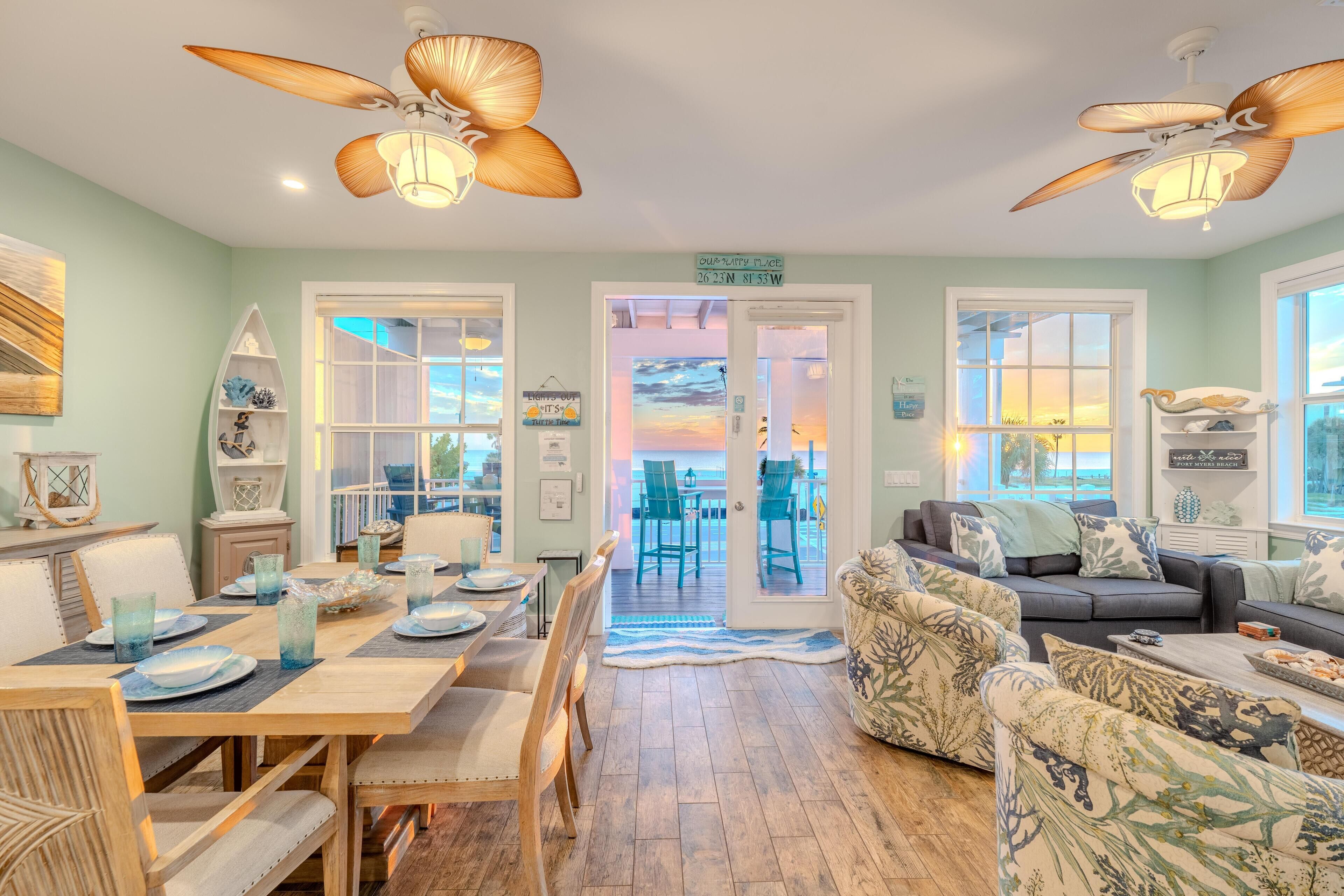 A spacious living room with a dining area, large windows, and ceiling fans.