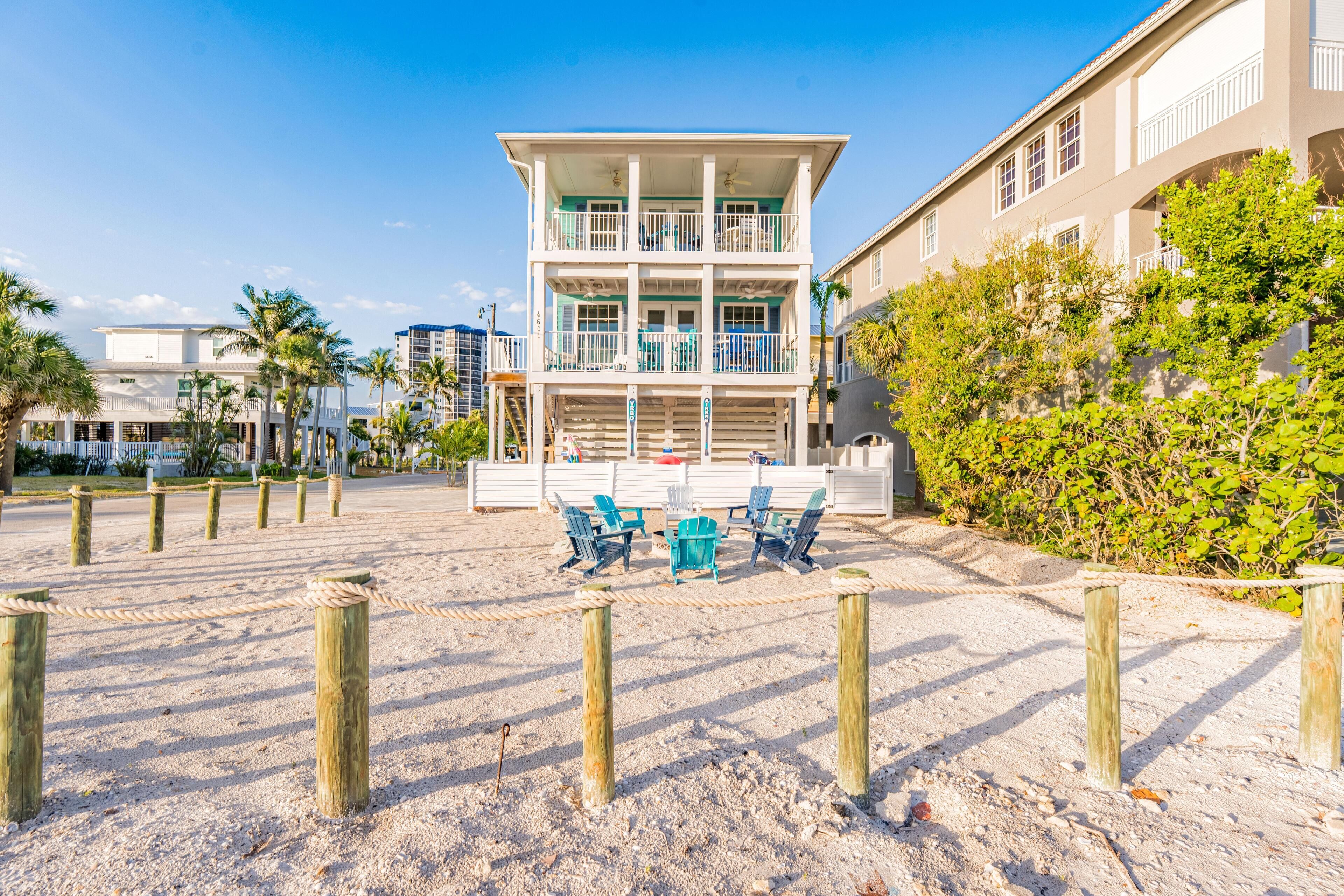 A beachfront property with a two-story building, outdoor seating area, and a sandy beach.