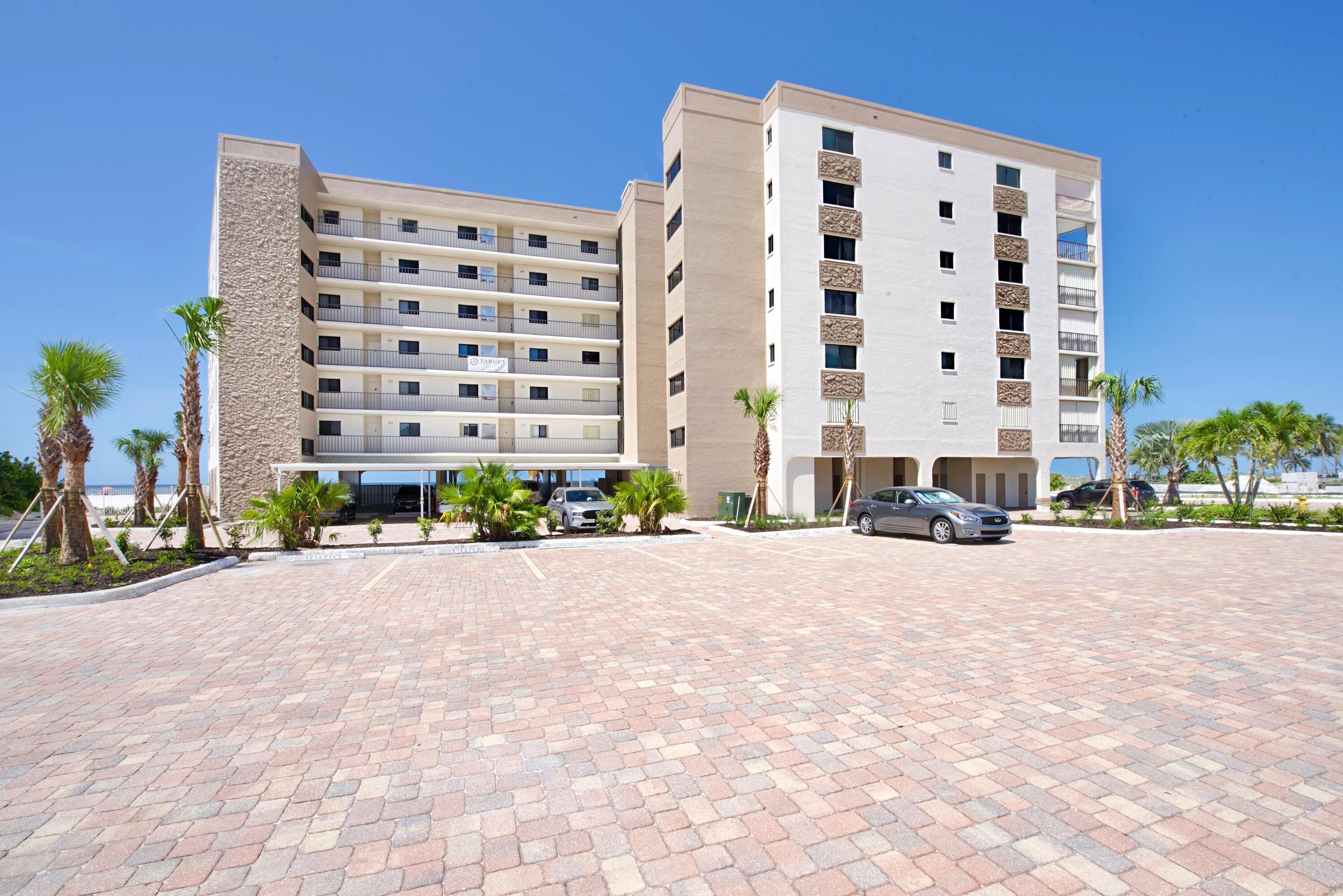 A multi-story hotel with a modern design, featuring a central courtyard with palm trees and a paved walkway.