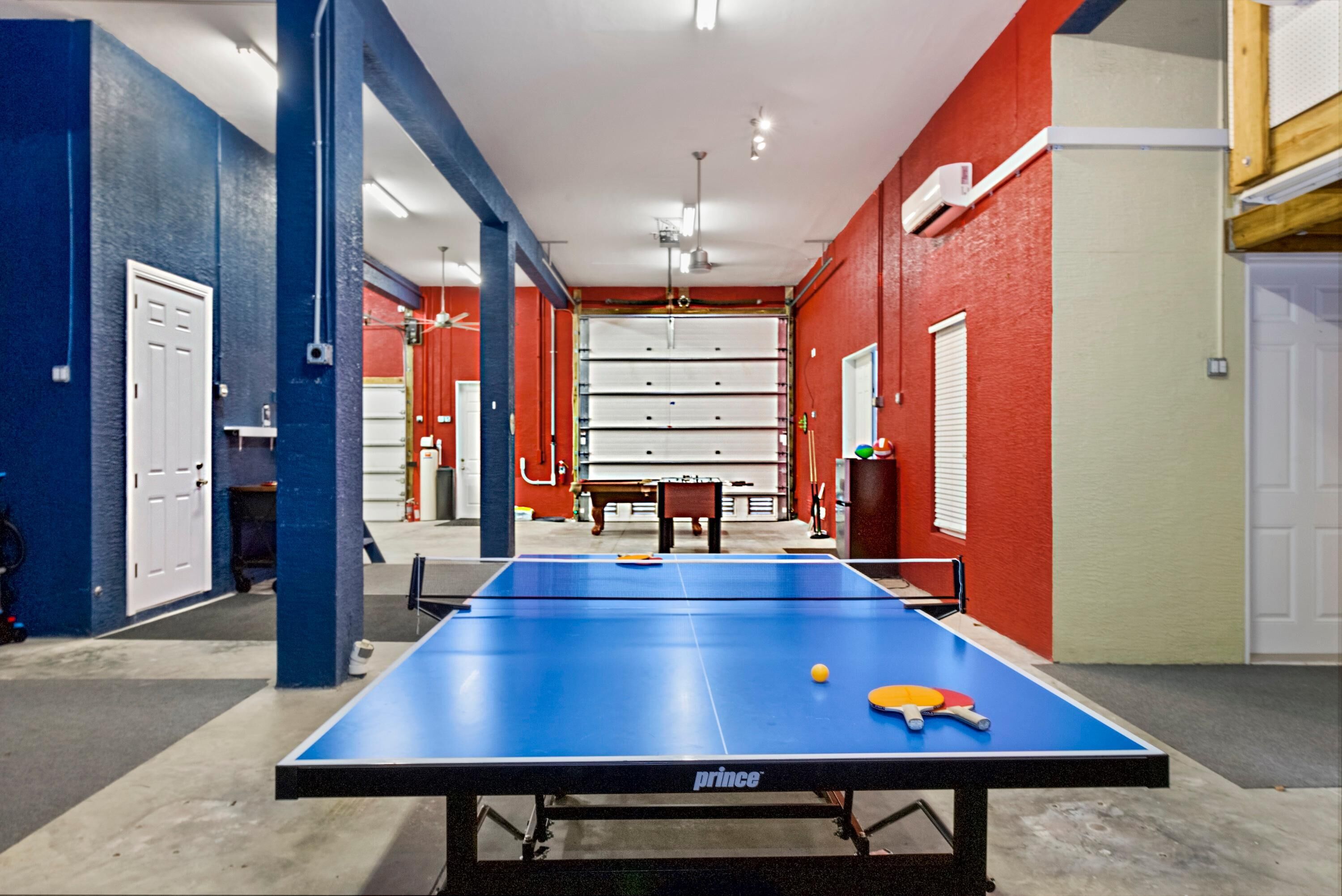 Ein Tischtennistisch mit blauer Spielfläche und weißem Netz, umgeben von roten Wänden und einem Deckenventilator.