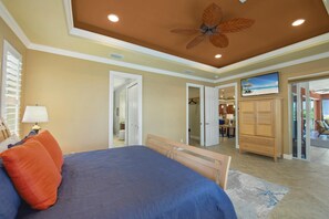 Quarto com cama, ventoinha no teto e vista para a sala de estar adjacente.