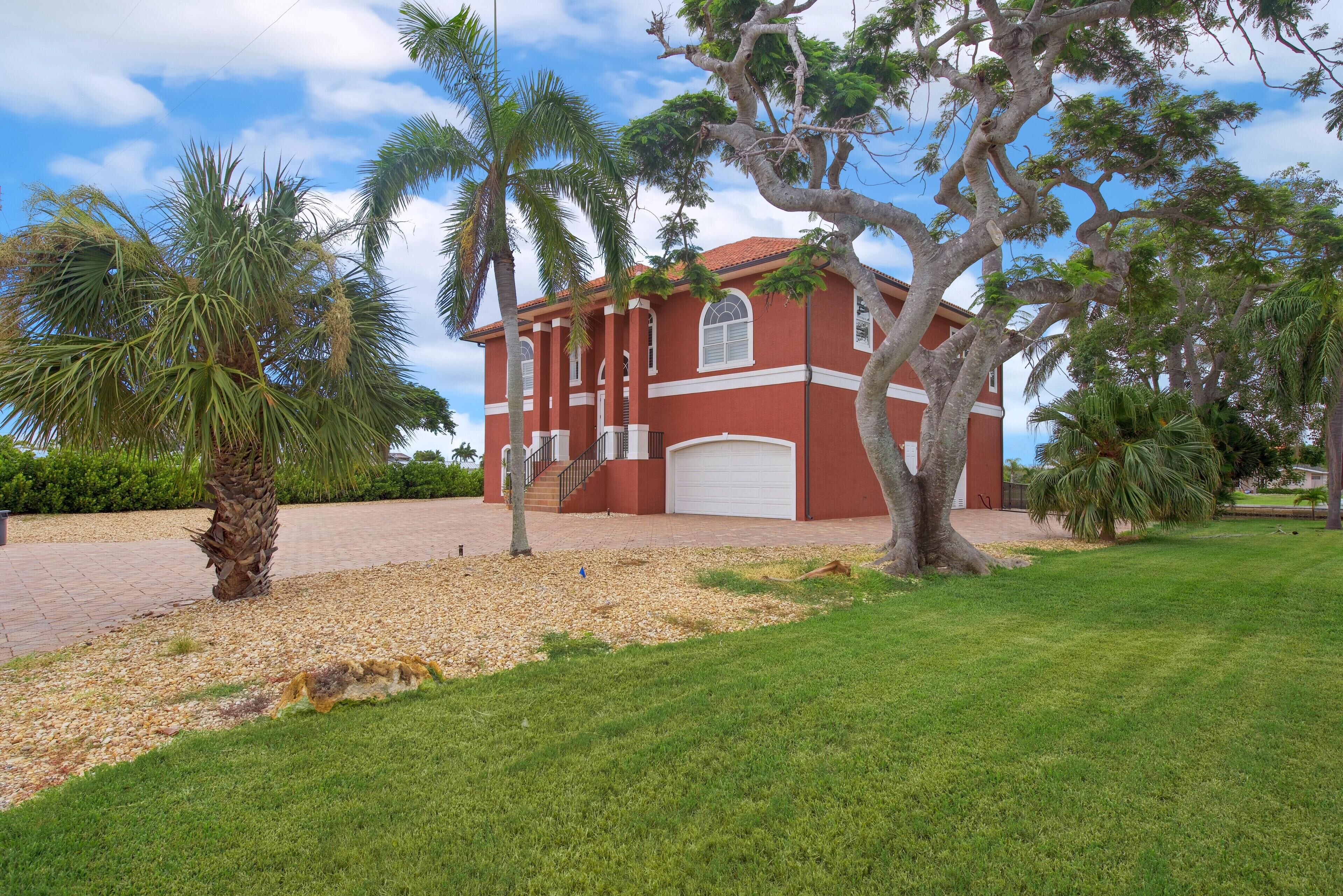 A red building with a white garage door, surrounded by palm trees and a grassy lawn.