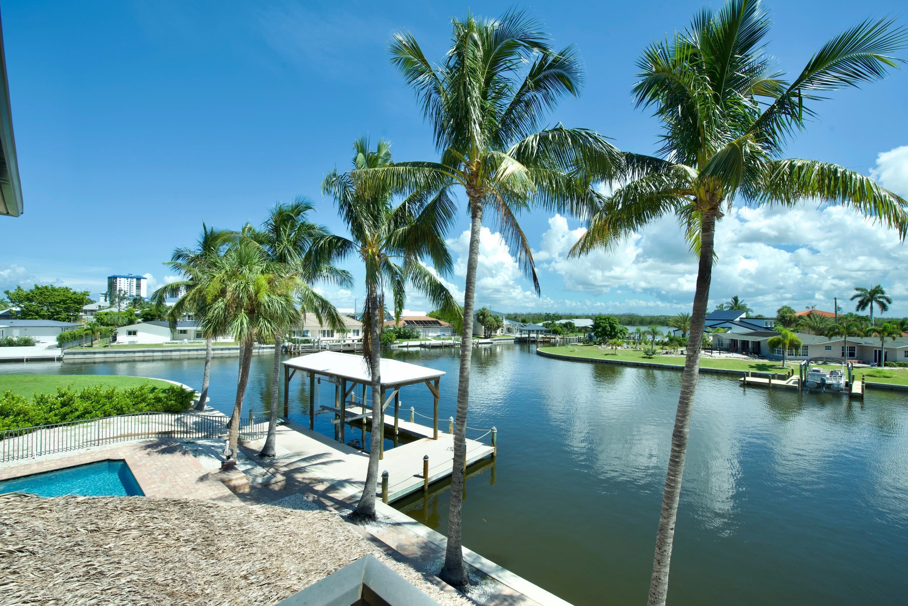 A waterfront property with a pool, palm trees, and a dock.