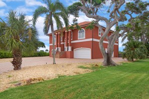 Um edifício vermelho com porta de garagem branca, rodeado por palmeiras e um gramado bem cuidado.