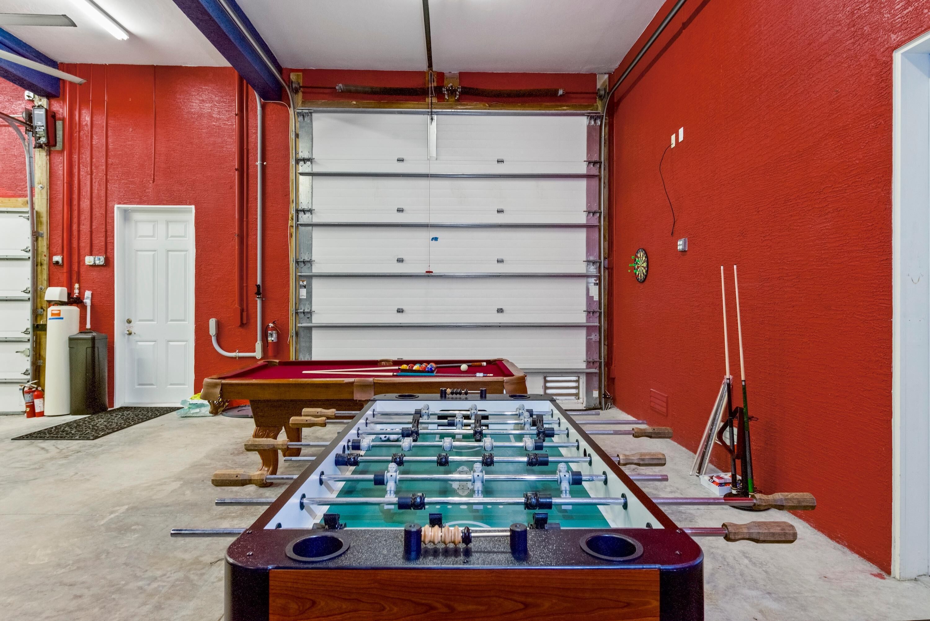A room with a foosball table, a pool table, and a red wall.