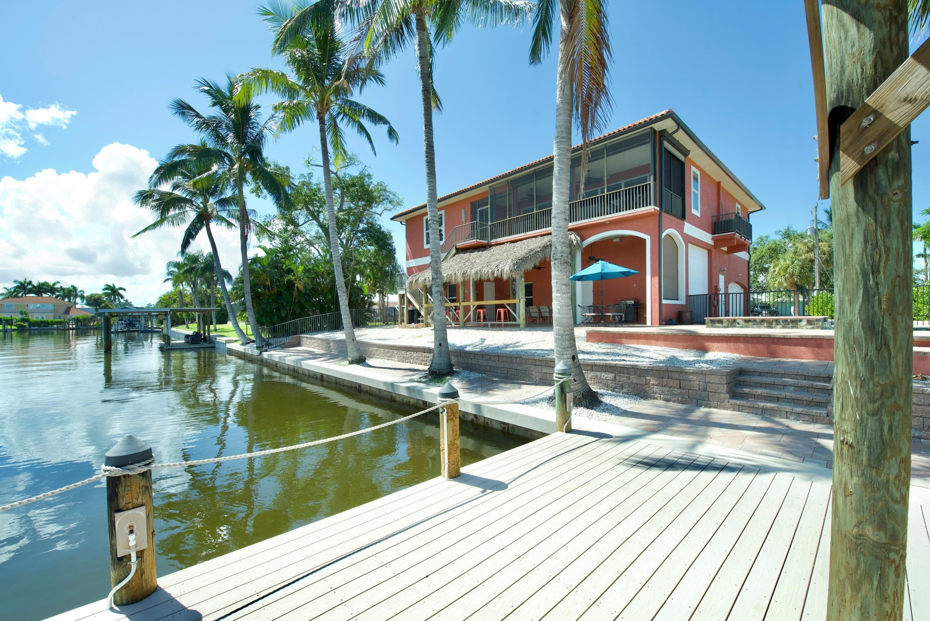 A waterfront property with a wooden dock, a thatched-roof structure, and a two-story building with balconies.