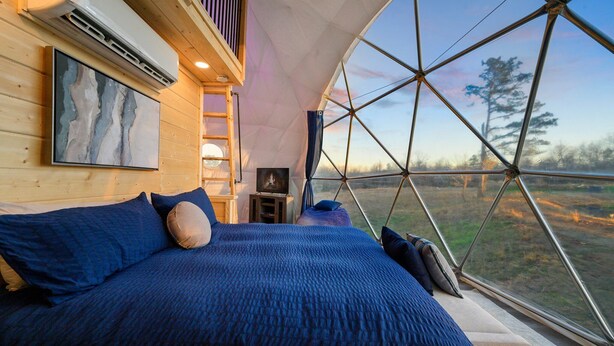 A cozy room with a large bed, a painting on the wall, and a view through a large window.