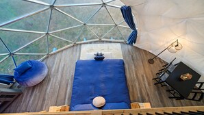 A geodesic dome room with a bed, a table, and a chair.
