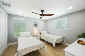 Two single beds with white mattresses and matching pillows, ceiling fan, and wall-mounted lamp.