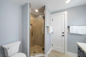Bathroom features a glass-enclosed shower, handheld showerhead, and a toilet with a visible tank.
