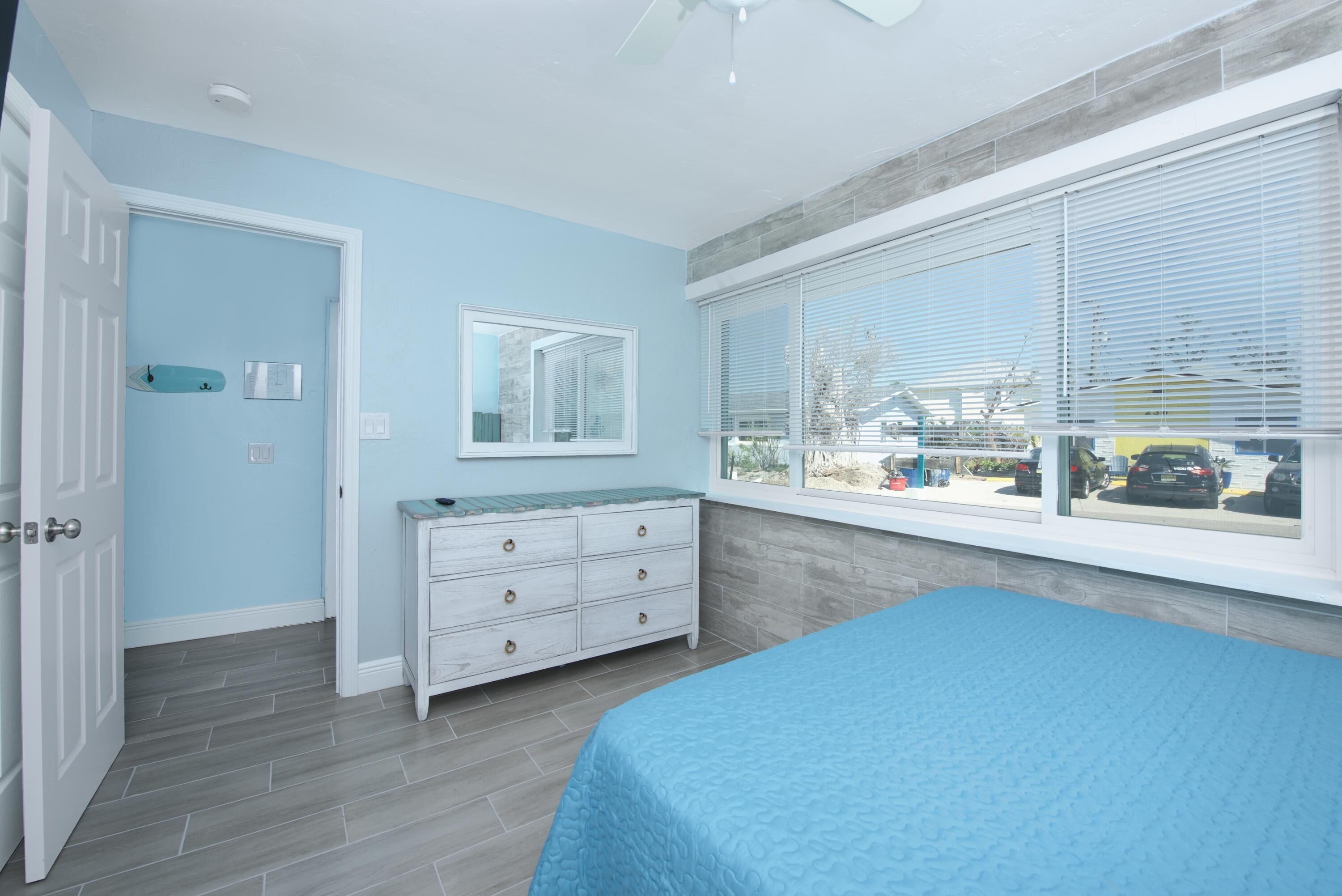A bedroom with a bed, a dresser, a window with blinds, and a door.