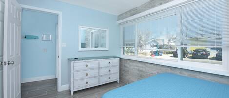 A bedroom with a bed, a dresser, a window with blinds, and a door.
