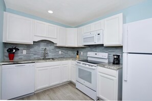 A modern kitchen with white cabinets, a microwave, a stove, and a dishwasher. - Mermaid Tales 3BR #1, #5, and #6 (Fort Myers Beach)