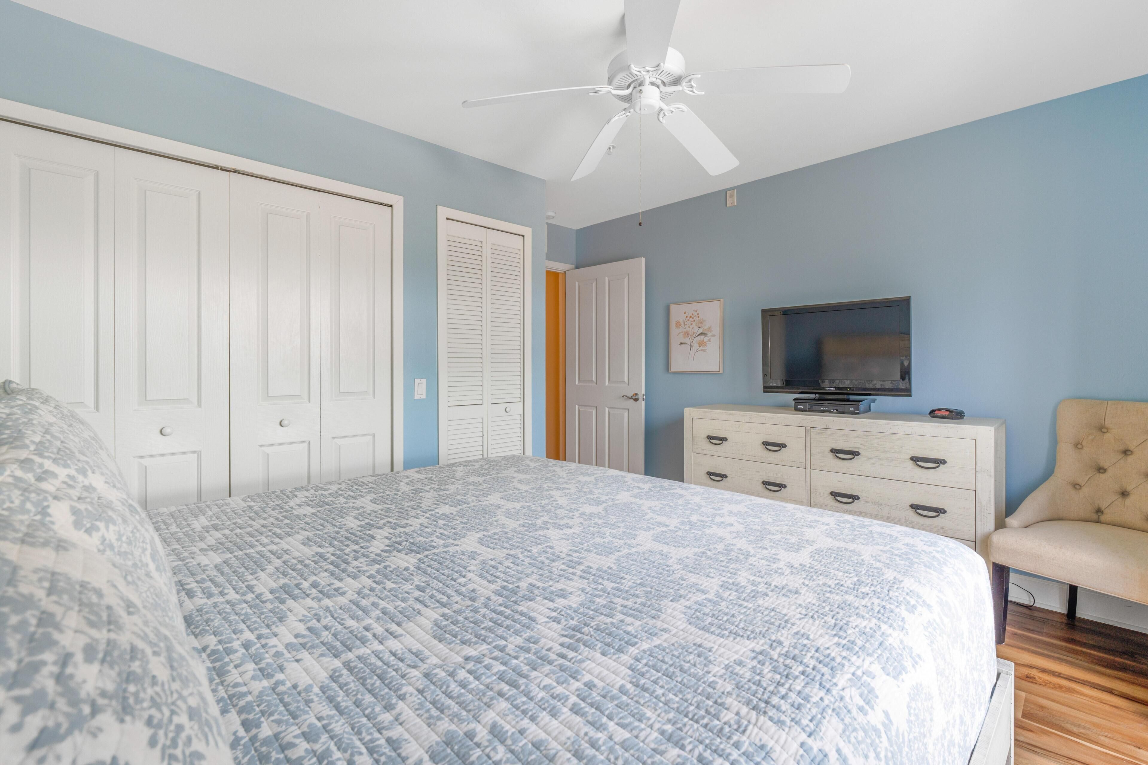 A bedroom with a bed, a ceiling fan, a dresser, a television, and a chair.