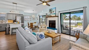 A spacious living area with a sofa, coffee table, and a fireplace. There is a balcony with outdoor furniture and a view of the sky.