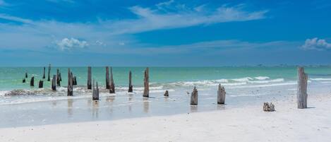 A beach with wooden posts and a lighthouse in the distance.