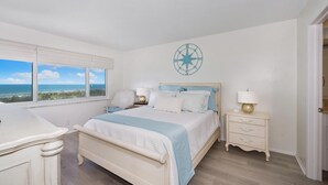 Una camera da letto con un letto, comodini, una sveglia a muro e una finestra vista oceano.