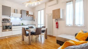 A modern kitchen with white cabinets, a dining table with chairs, a built-in oven, and a pendant light.