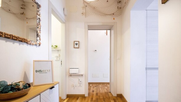 A hallway with wooden flooring, a framed sign on a counter, and a door at the end.
