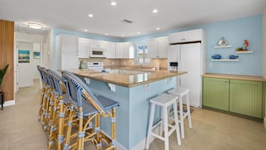 A modern kitchen with white cabinets, a central island with bar stools, and a green accent wall. - Endless Tides 1 (Fort Myers Beach)