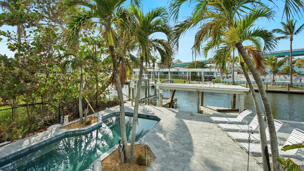 A pool area with palm trees, lounge chairs, and a bridge over water.