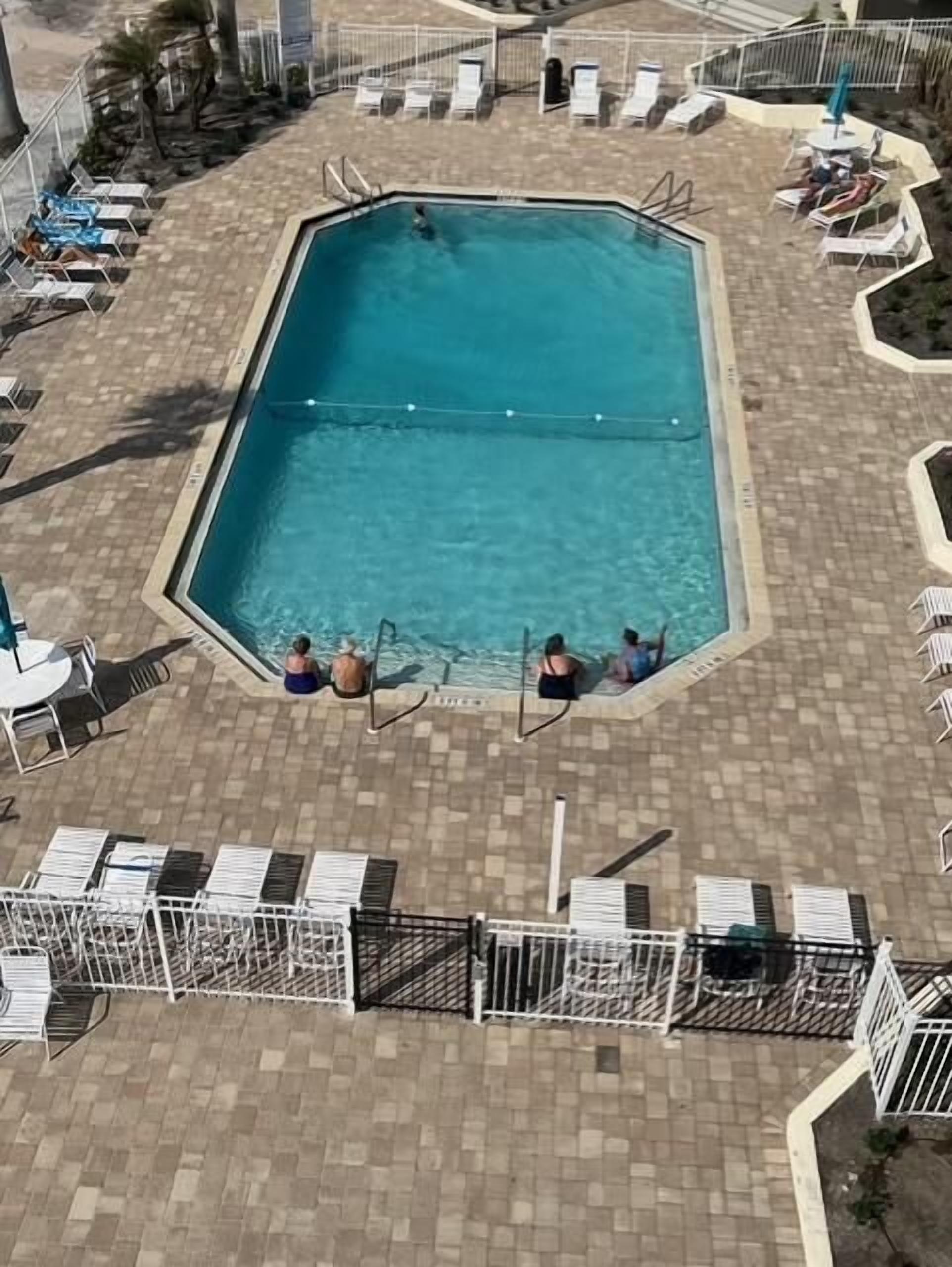 A rectangular pool with a tiled deck surrounding it, equipped with lounge chairs and a small table.