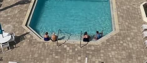 A rectangular pool with a tiled deck surrounding it, equipped with lounge chairs and a small table.