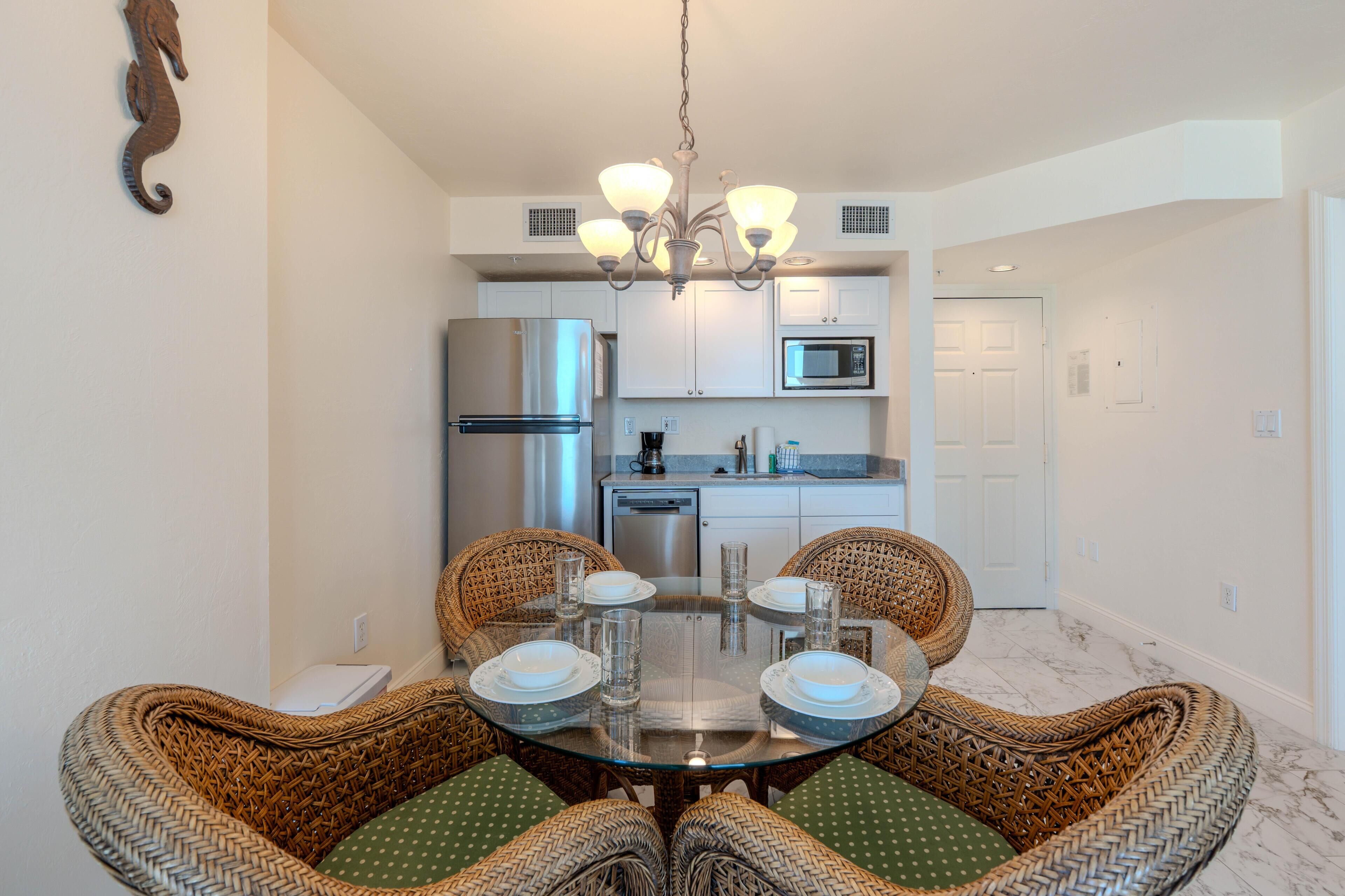 A modern kitchen with stainless steel appliances, a dining area with wicker chairs, and a chandelier.