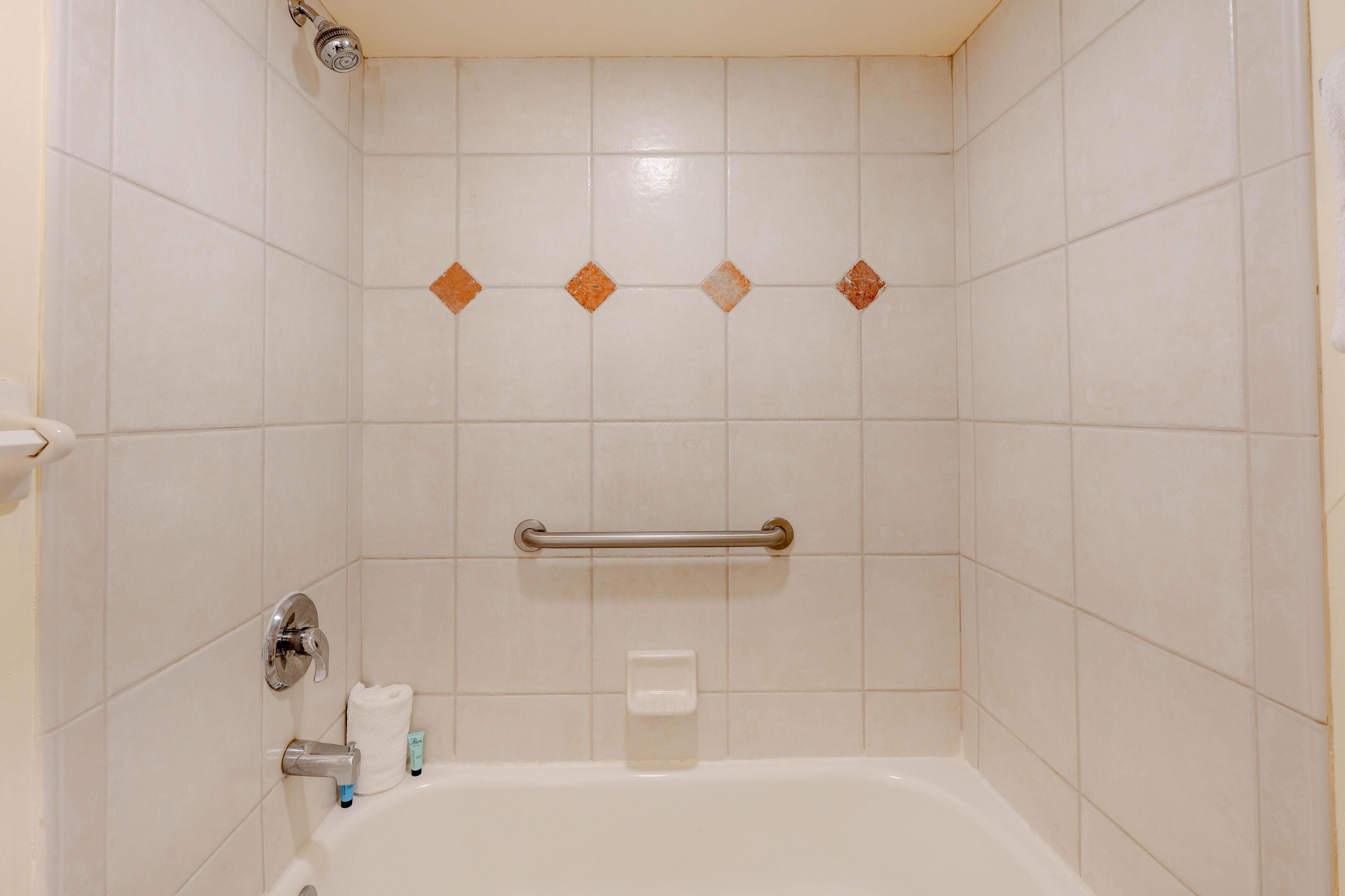 Un baño con bañera, barras de apoyo, una toalla y artículos de aseo.