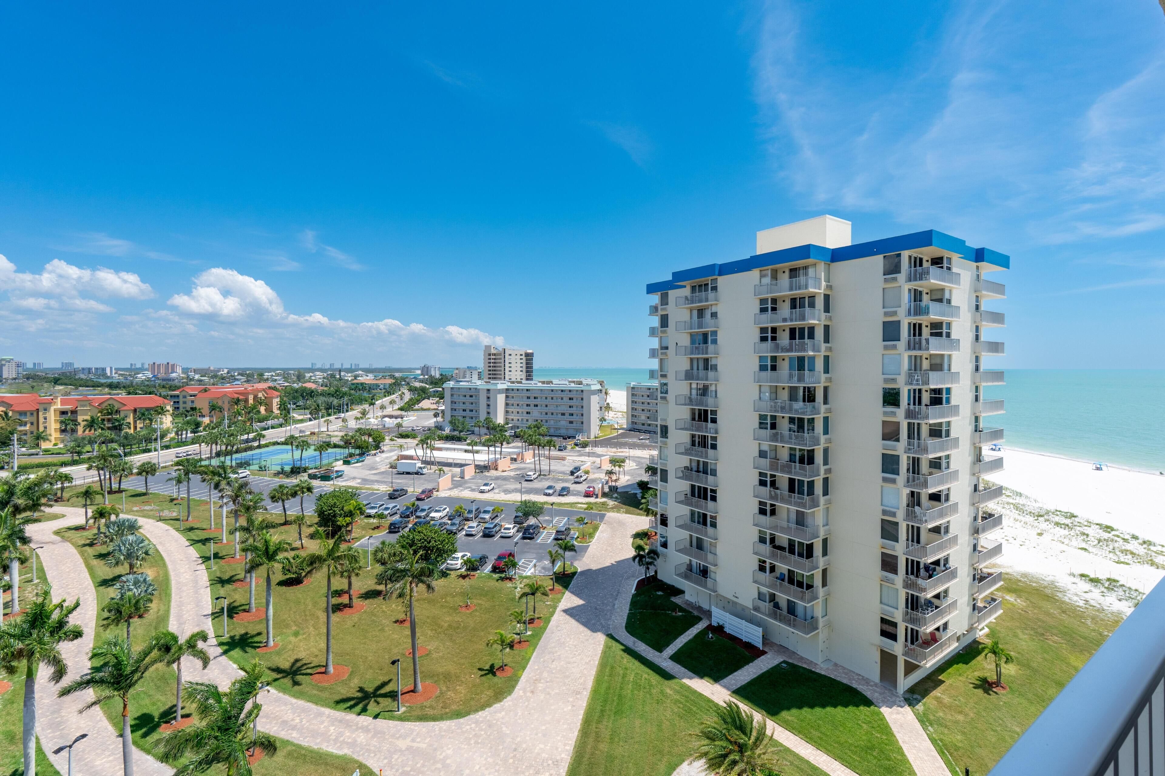 A high-rise hotel with a pool, beachfront view, and a parking lot.