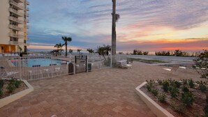A pool area with lounge chairs, a tall palm tree, and a sunset view.
