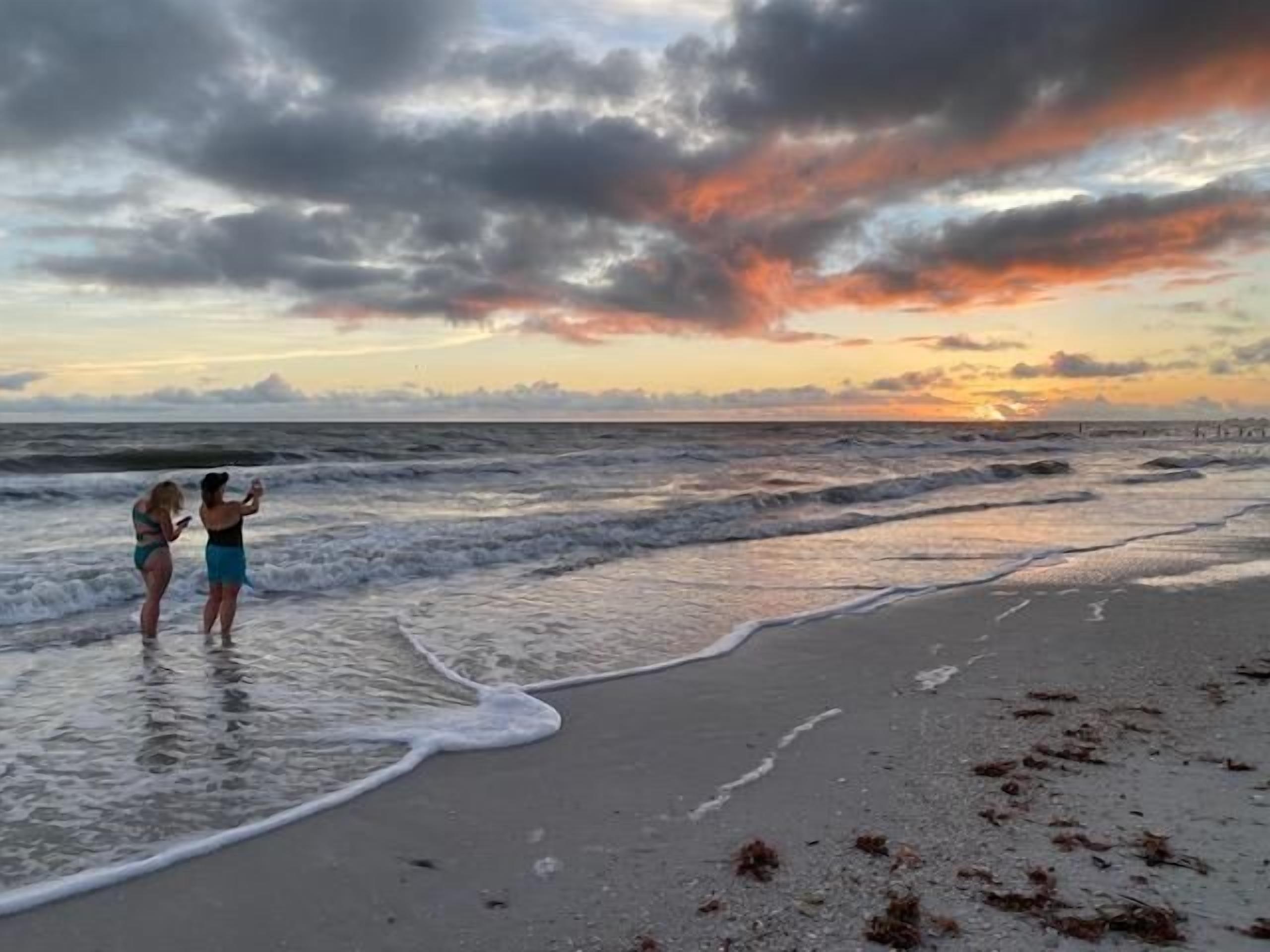 Een strandscène met twee mensen die in ondiep water staan, de oceaan tegemoet.