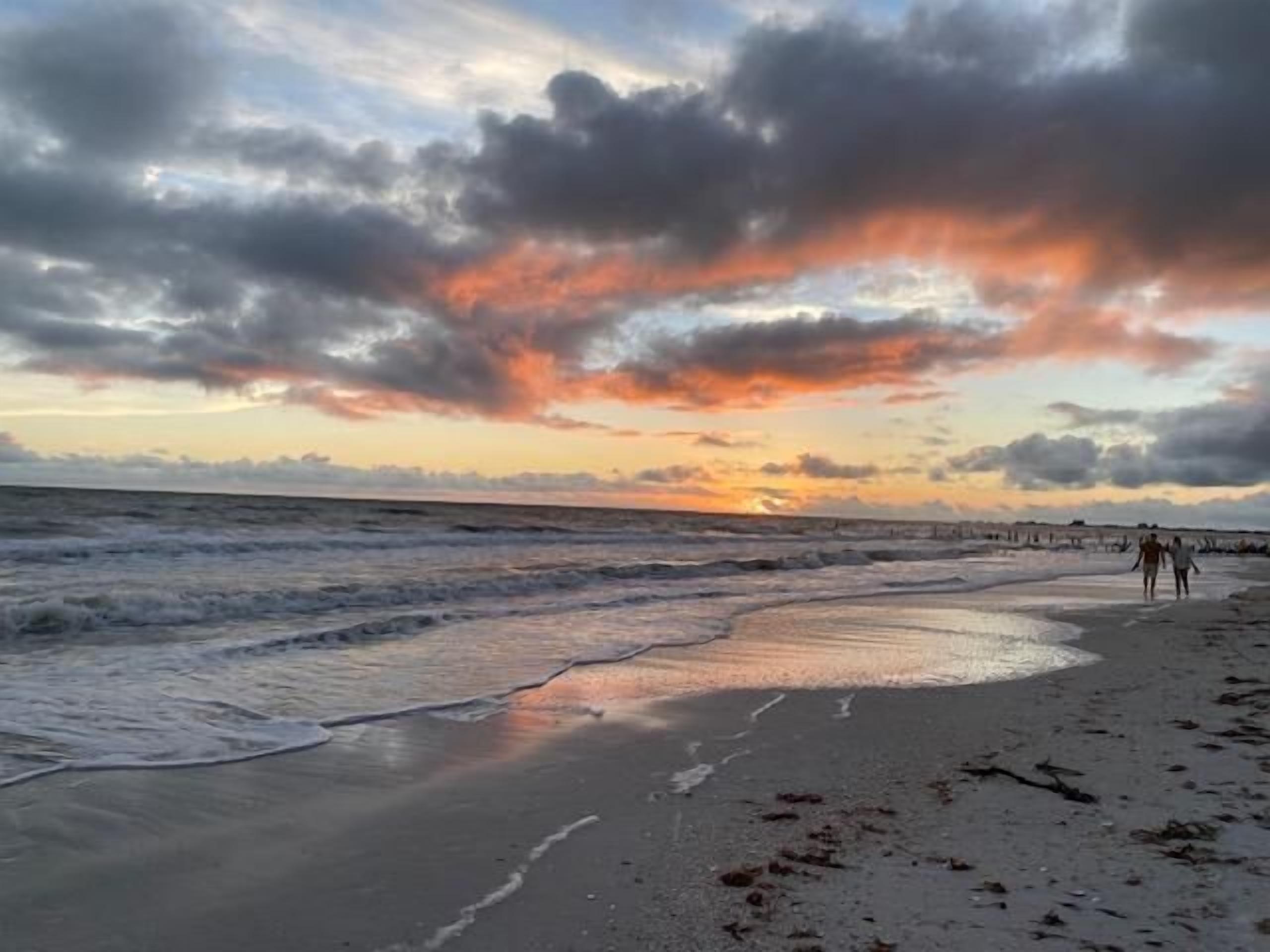 A beach with waves, a sunset, and a cloudy sky.