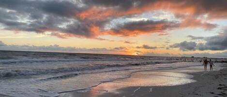 A beach with waves, a sunset, and a cloudy sky.