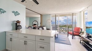 A modern kitchen with white cabinets, a coffee maker, and a dining area with a red chair and a pool view.