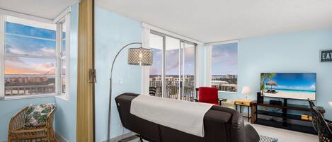 A modern living room with a sofa, a red chair, a TV, and a view of a cityscape through large windows.