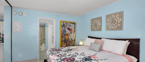 A bedroom with a floral bedspread, a wooden headboard, and two wall art pieces.