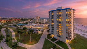 A high-rise hotel with multiple balconies, a pool, and a view of the beach at sunset.