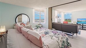 A bedroom with a bed, a desk, a chair, a TV, and a balcony with a view.